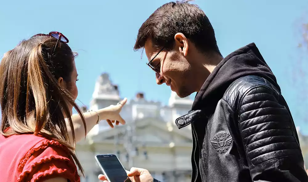 young couple with mobile phones during a themed city tour in downtown Budapest is pointing into the distance