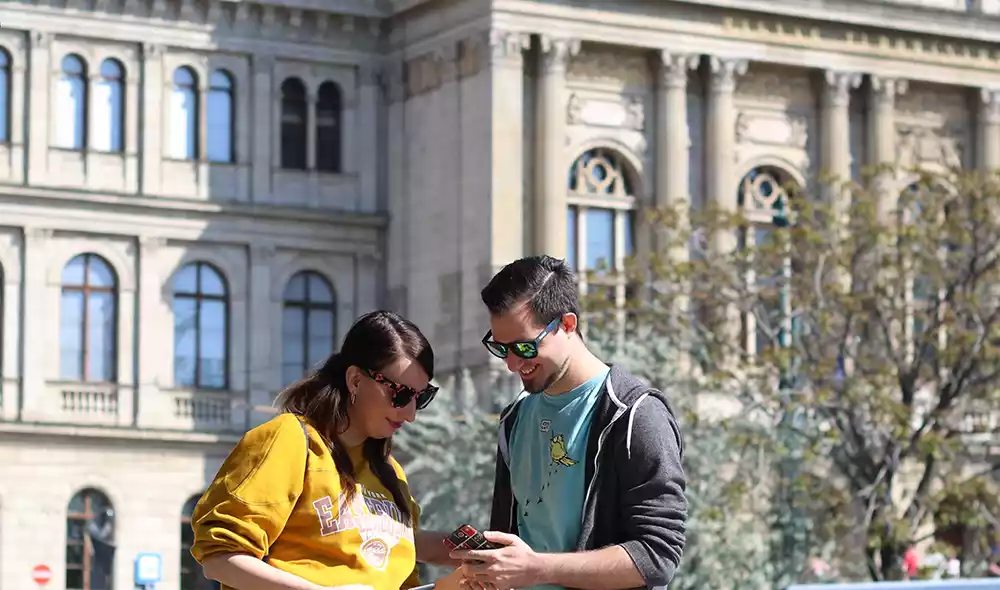 young couple wearing sunglasses are playing a Landventure adventure game on their mobile phones in Budapest