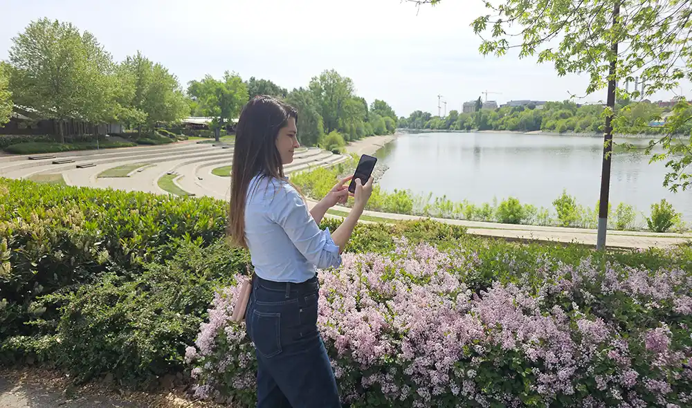 a young woman at BudaPart holding a smartphone and playing the Landventure outdoor detective game