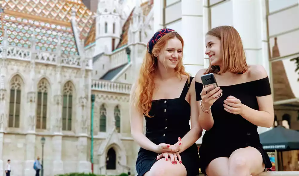 two girls are playing Landventure scavenger hunt on their mobile phones in the Buda Castle District