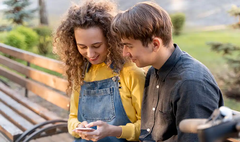 a young couple sitting on a bench and playing a Landventure outdoor escape game with a smartphone in downtown Debrecen