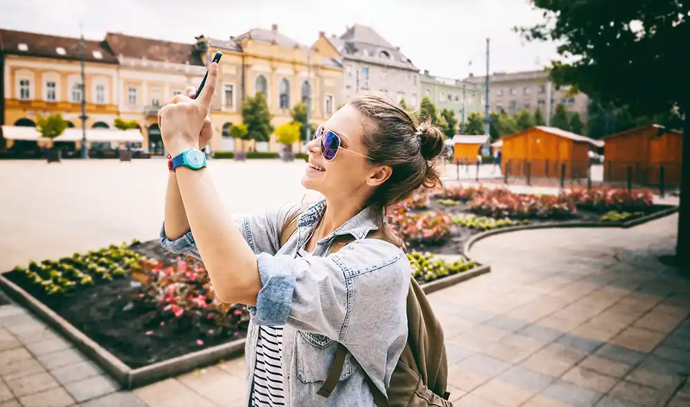 egy fiatal nő okostelefonját a magasba emelve Landventure szabadtéri szabadulós játékot játszik Debrecen belvárosában