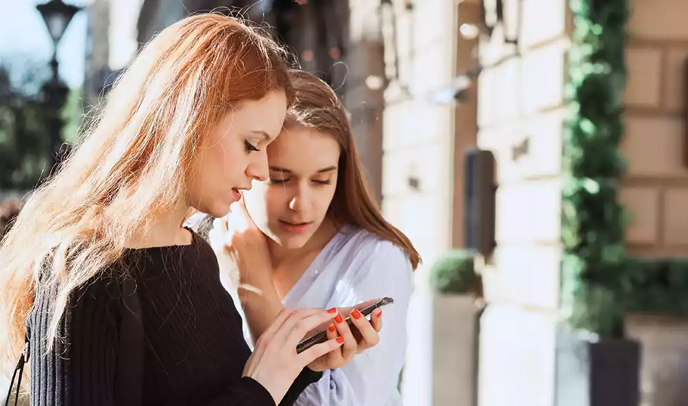two girls are deeply focused on a smartphone in downtown Esztergom while playing a city adventure game