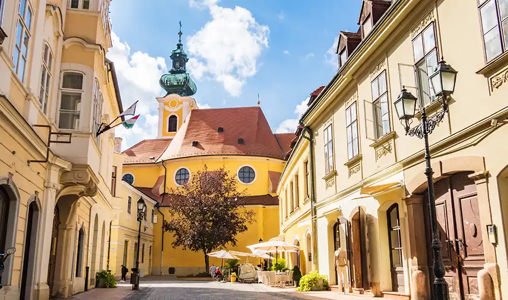 a győri Kazinczy utca napsütésben, háttérben a Karmelhegyi Boldogasszony-templommal – egy Landventure küldetés helyszíne