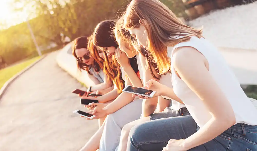 egy lánycsapat Kecskeméten üldögélve Landventure szabadtéri szabadulós játékot játszik okostelefonon