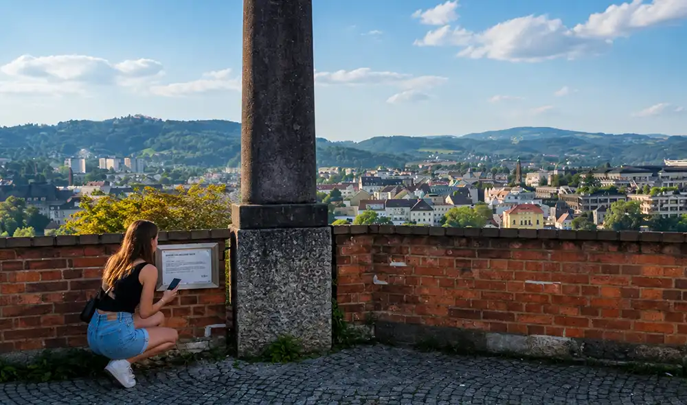 woman solving a Landventure outdoor escape mission at a viewpoint over Linz with her smartphone