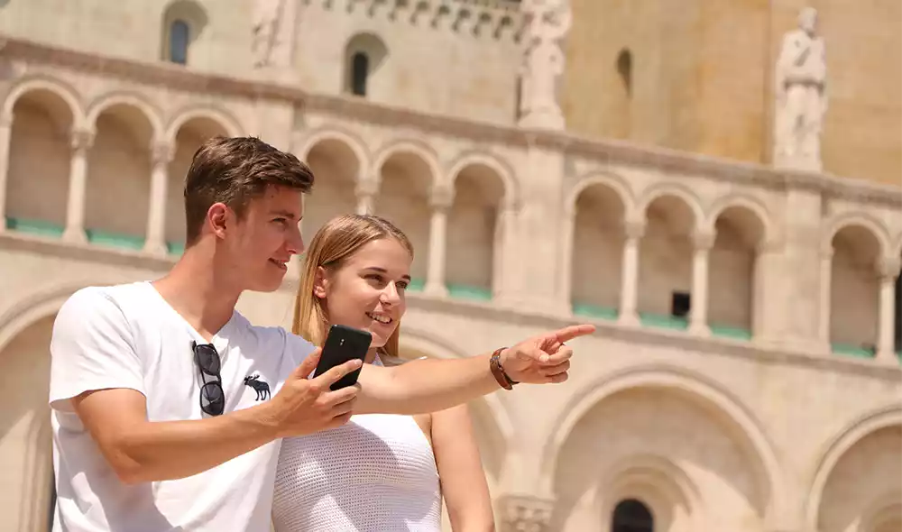 a young couple in downtown Pécs pointing into the distance while playing the Landventure detective game on a smartphone