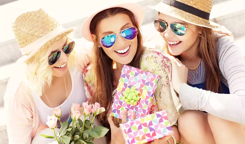 experience gift ideas for women: three smiling women in hats giving each other presents
