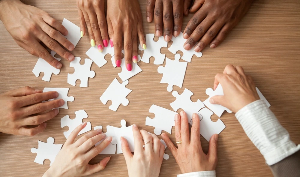a group of coworkers taking part in a team building game – only their hands are visible as they piece together a puzzle
